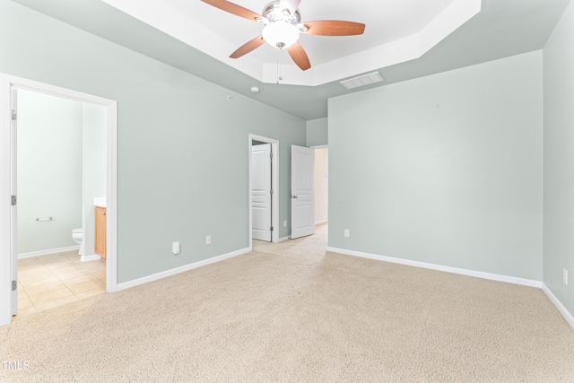 unfurnished bedroom with baseboards, a tray ceiling, light tile patterned flooring, light carpet, and connected bathroom