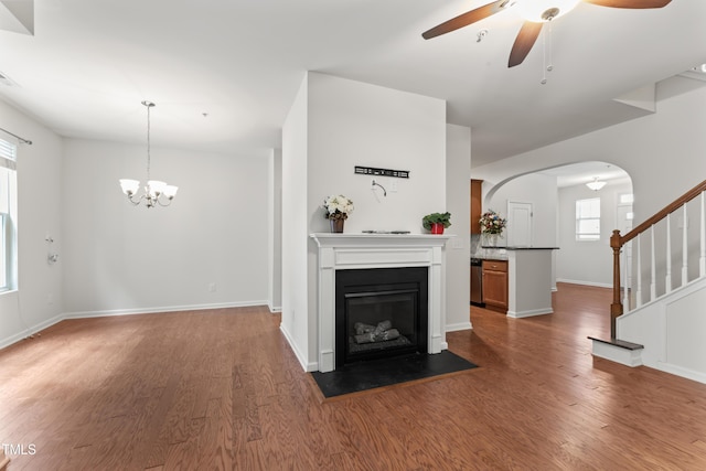 unfurnished living room featuring ceiling fan with notable chandelier, stairway, a fireplace with flush hearth, and wood finished floors