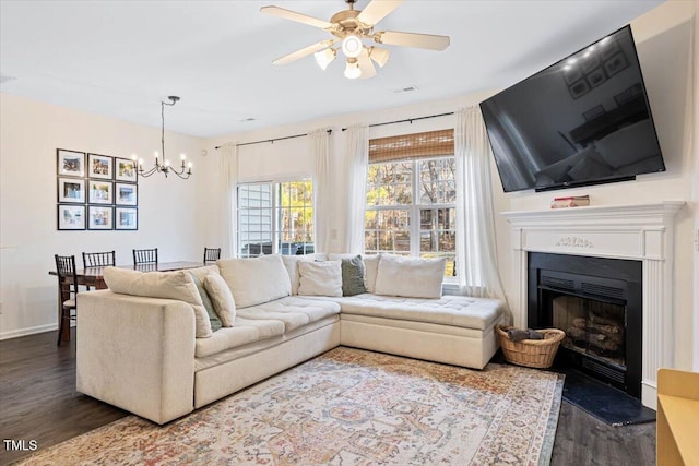 living area featuring dark wood-style floors, visible vents, baseboards, a fireplace with raised hearth, and ceiling fan with notable chandelier