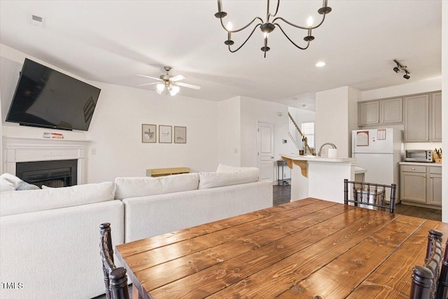 dining area featuring visible vents, a toaster, stairway, ceiling fan with notable chandelier, and a fireplace