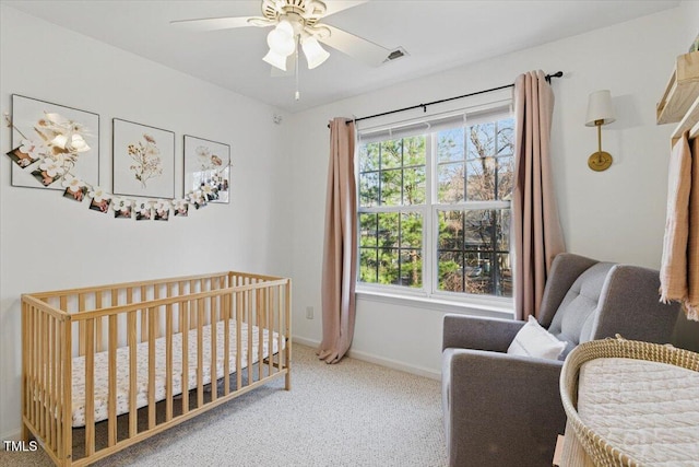 carpeted bedroom featuring visible vents, baseboards, a crib, and a ceiling fan