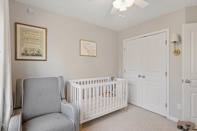 bedroom with baseboards, ceiling fan, a crib, a closet, and light carpet