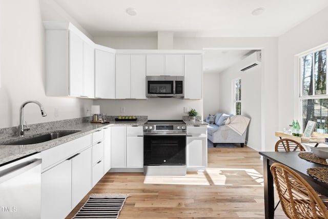 kitchen featuring light stone counters, light wood-style flooring, appliances with stainless steel finishes, white cabinetry, and a sink