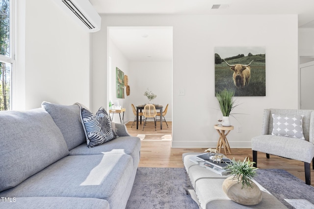 living room featuring visible vents, baseboards, wood finished floors, and a wall unit AC