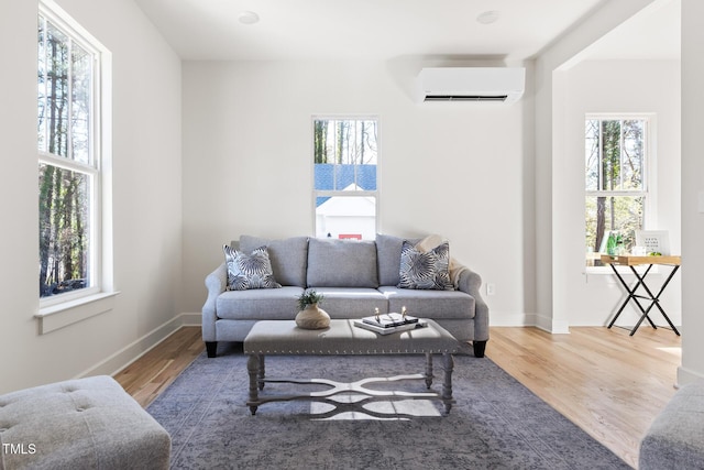 living room with baseboards, plenty of natural light, wood finished floors, and a wall unit AC