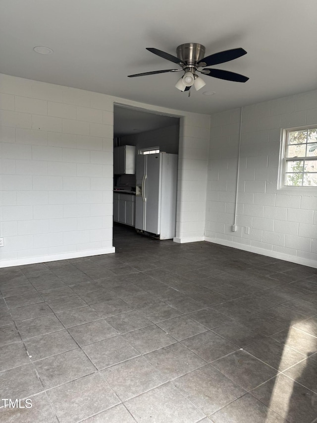 spare room with a ceiling fan and concrete block wall