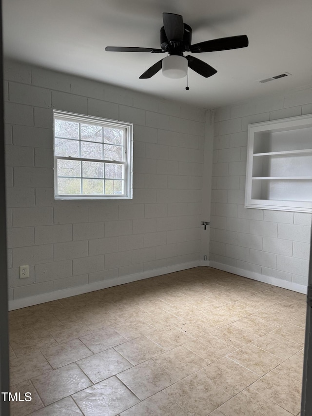 spare room with visible vents, ceiling fan, and concrete block wall