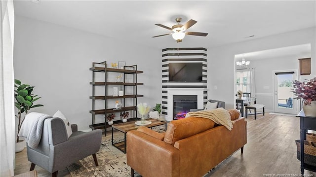 living room featuring a large fireplace, wood finished floors, and ceiling fan with notable chandelier