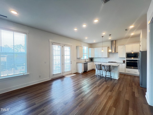 kitchen with a sink, appliances with stainless steel finishes, wall chimney exhaust hood, and white cabinets