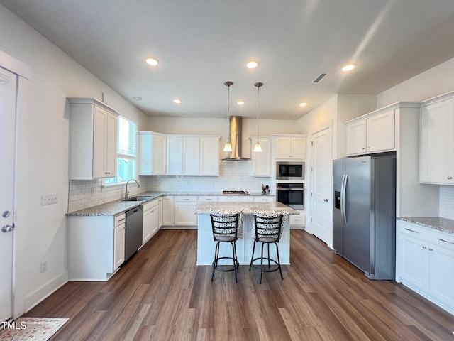 kitchen featuring visible vents, a sink, stainless steel appliances, wall chimney exhaust hood, and a center island