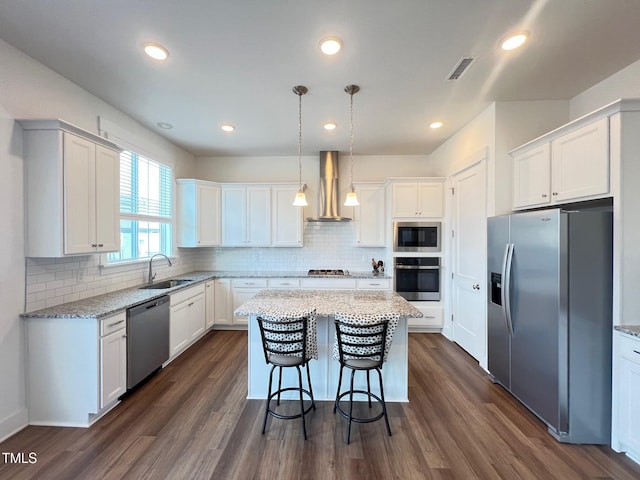 kitchen with visible vents, wall chimney range hood, appliances with stainless steel finishes, white cabinets, and a sink