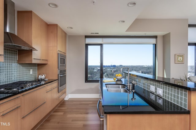 kitchen featuring visible vents, a sink, backsplash, appliances with stainless steel finishes, and wall chimney exhaust hood