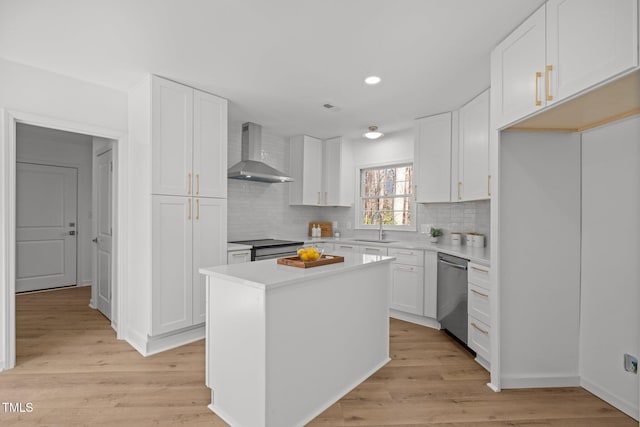 kitchen with light wood finished floors, dishwasher, white cabinets, wall chimney exhaust hood, and a sink