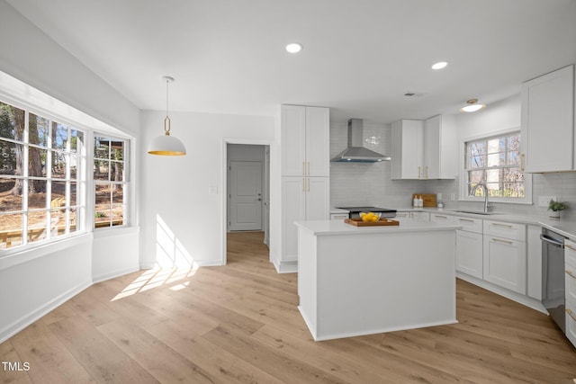 kitchen featuring decorative backsplash, wall chimney exhaust hood, light wood finished floors, and a sink