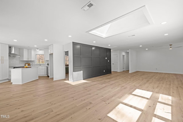 unfurnished living room with a skylight, recessed lighting, visible vents, and light wood-type flooring