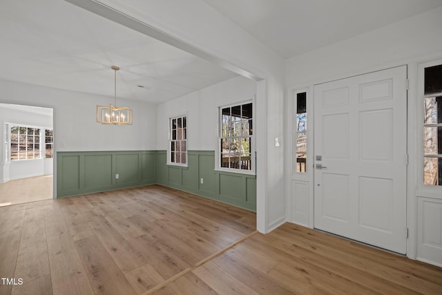 foyer entrance with light wood finished floors, a notable chandelier, and a wainscoted wall