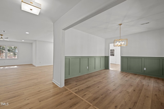 unfurnished room featuring visible vents, ceiling fan with notable chandelier, a decorative wall, and light wood finished floors