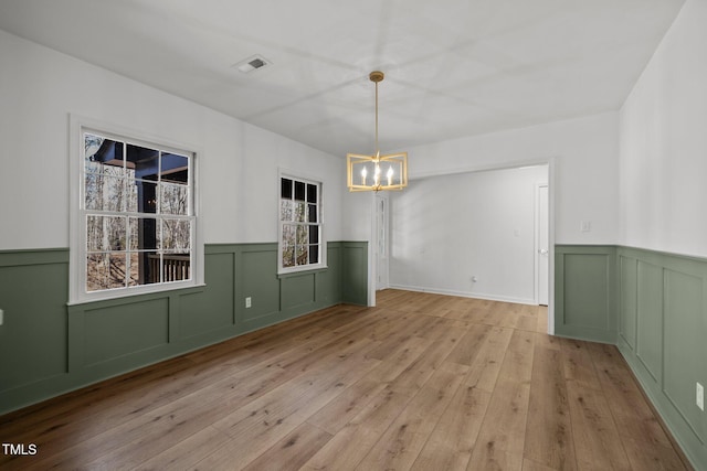 unfurnished dining area featuring visible vents, light wood-style floors, an inviting chandelier, and a wainscoted wall