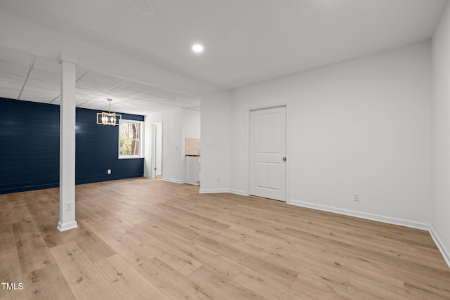 basement featuring light wood-style floors, baseboards, and a chandelier