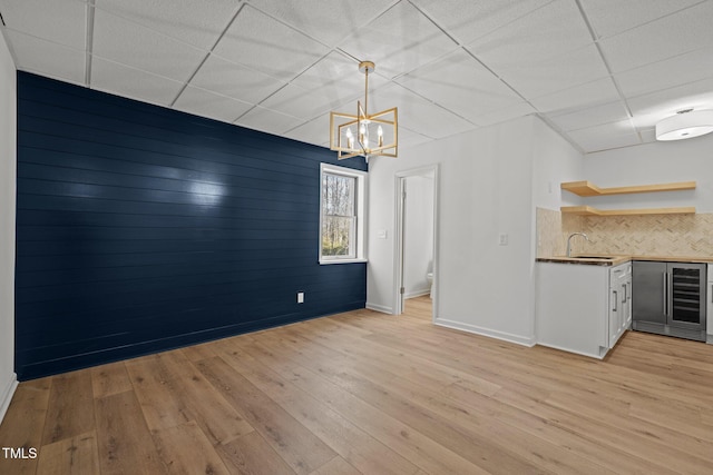 unfurnished dining area with a sink, a notable chandelier, light wood-style floors, and indoor wet bar