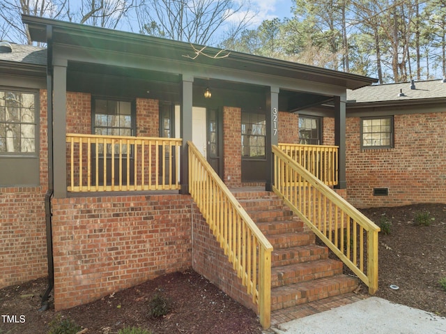 doorway to property with a shingled roof, covered porch, brick siding, and crawl space