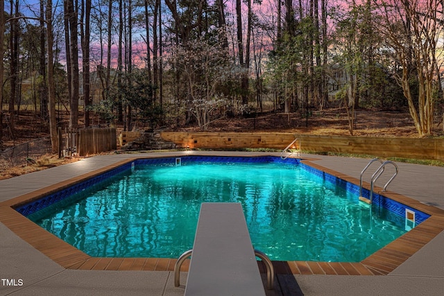 pool at dusk with a fenced in pool, fence, and a diving board