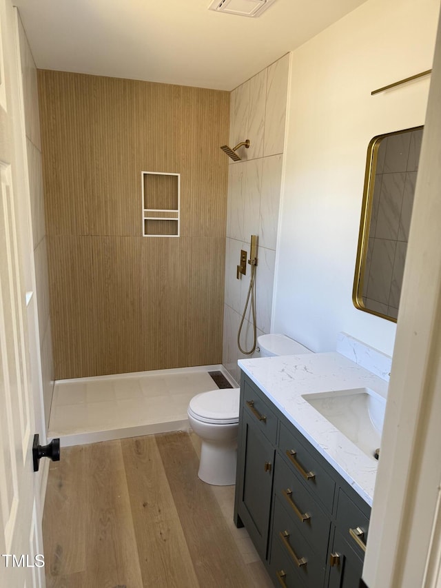 bathroom featuring vanity, wood finished floors, visible vents, tiled shower, and toilet