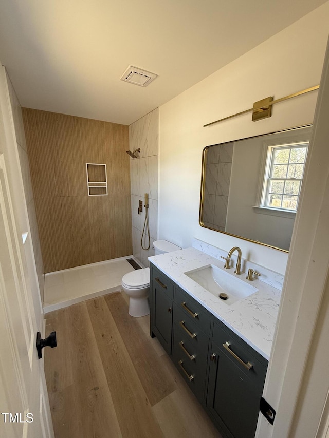 full bath with tiled shower, toilet, vanity, and wood finished floors