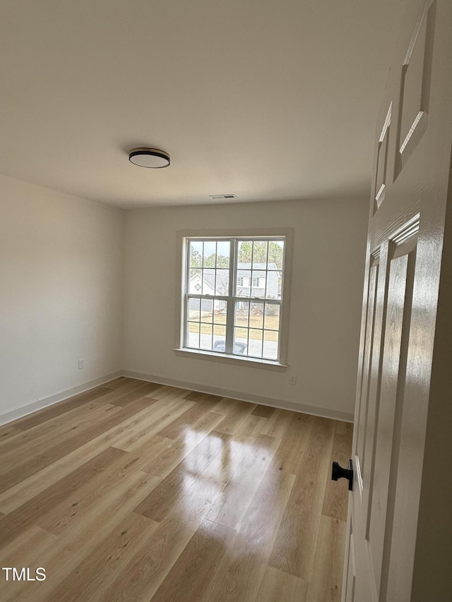 unfurnished room with light wood finished floors, visible vents, and baseboards