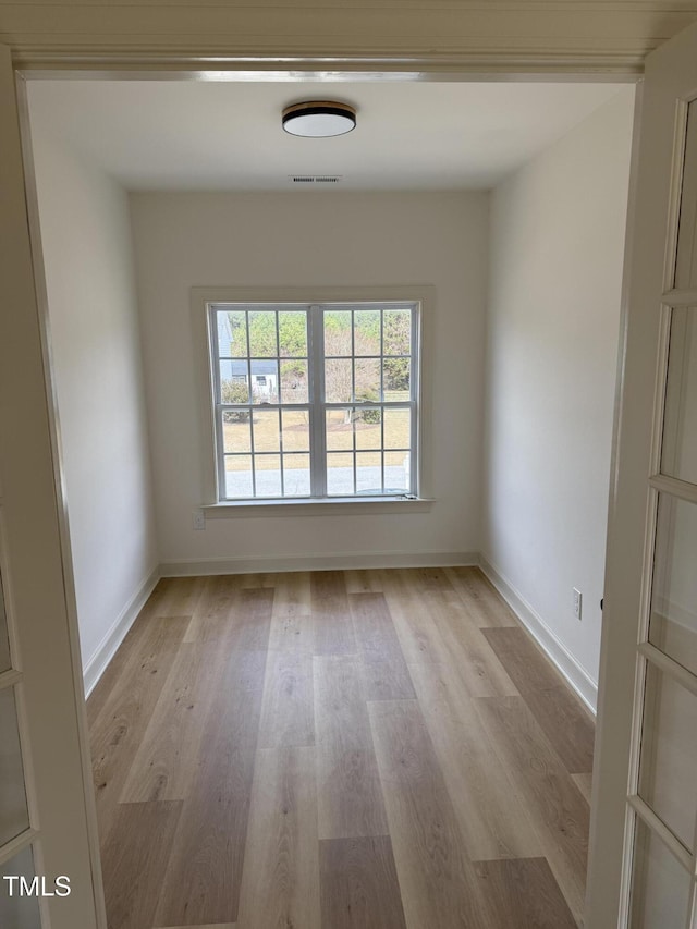 unfurnished room with light wood-style floors, visible vents, a wealth of natural light, and baseboards