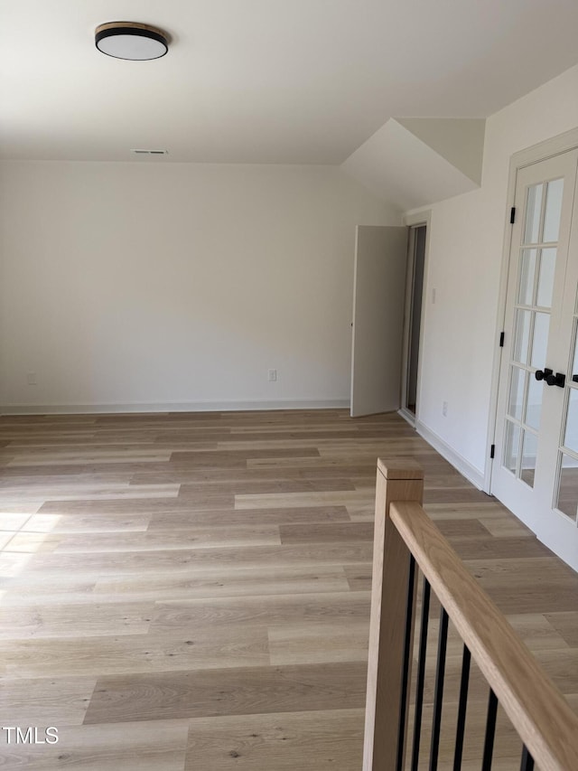 spare room with visible vents, baseboards, light wood-style floors, and vaulted ceiling