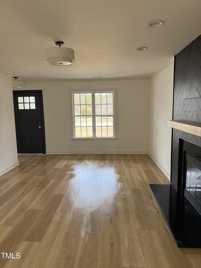 unfurnished living room featuring crown molding, a fireplace, baseboards, and light wood finished floors