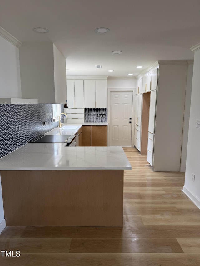 kitchen with light wood-type flooring, a sink, a peninsula, black cooktop, and decorative backsplash