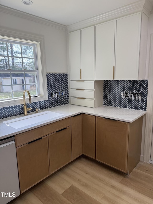 kitchen with light wood finished floors, light countertops, dishwashing machine, white cabinets, and a sink