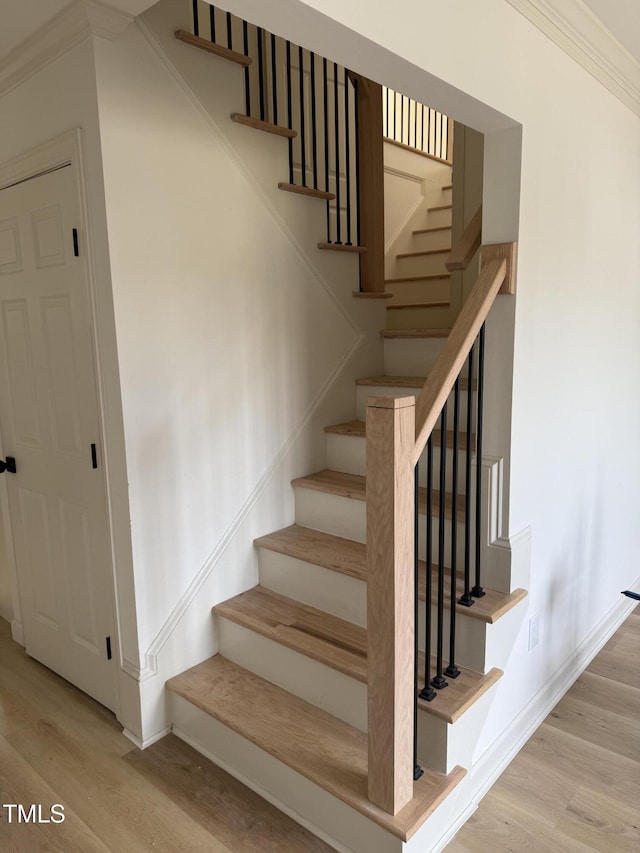 staircase featuring crown molding, wood finished floors, and baseboards