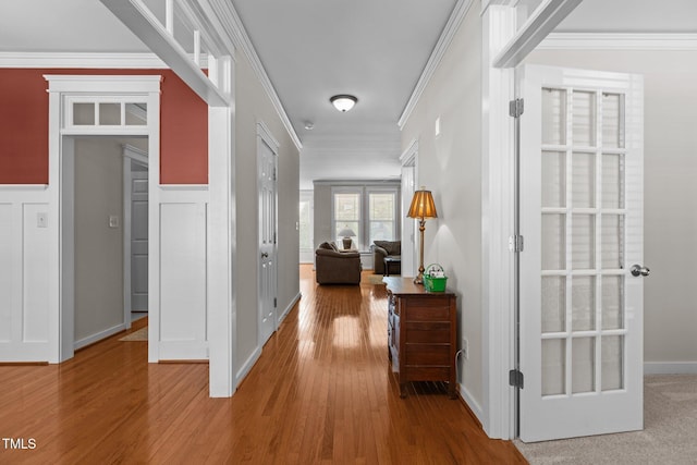 corridor with a wainscoted wall, wood finished floors, crown molding, and a decorative wall