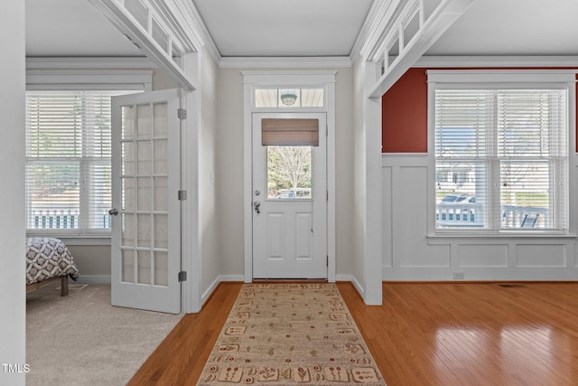 entrance foyer featuring a decorative wall, plenty of natural light, light wood finished floors, and crown molding