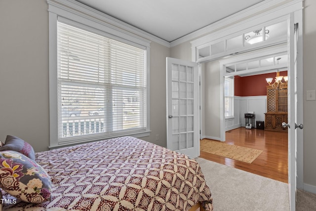 carpeted bedroom with french doors, wood finished floors, a chandelier, and crown molding