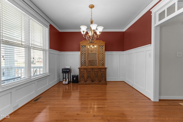 dining area featuring wood finished floors, visible vents, ornamental molding, a decorative wall, and a notable chandelier