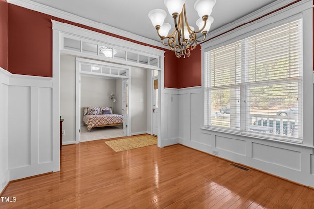 interior space with visible vents, light wood-style flooring, wainscoting, a decorative wall, and a notable chandelier