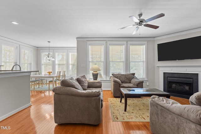 living room featuring a ceiling fan, baseboards, light wood finished floors, a fireplace, and crown molding