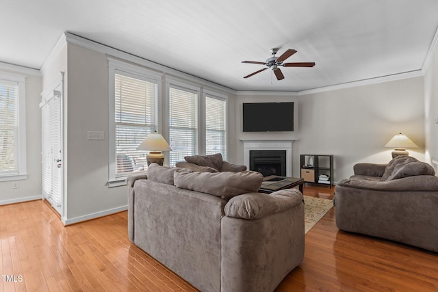 living room featuring baseboards, ceiling fan, ornamental molding, a fireplace, and light wood-style floors