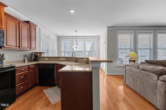 kitchen with light wood finished floors, open floor plan, a peninsula, black appliances, and a sink