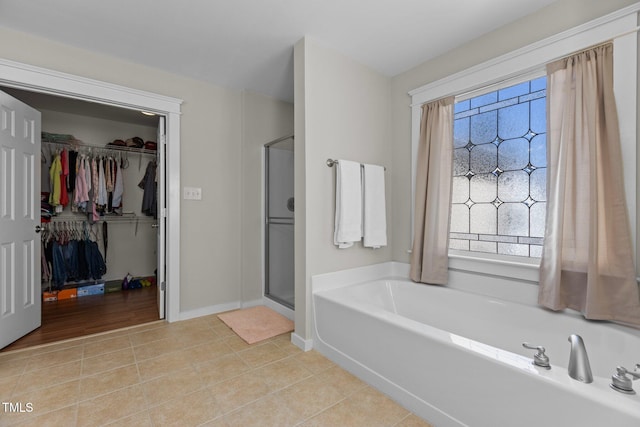 bathroom featuring baseboards, tile patterned flooring, a shower stall, a walk in closet, and a bath