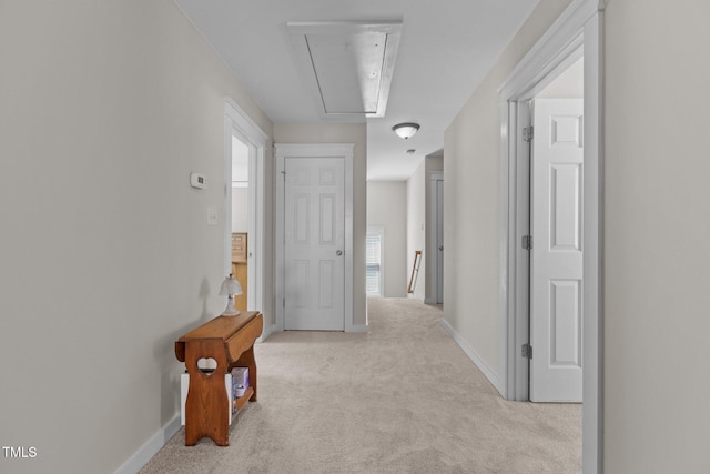 hall featuring attic access, light colored carpet, and baseboards