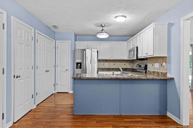 kitchen with dark wood finished floors, a peninsula, stainless steel appliances, white cabinets, and tasteful backsplash