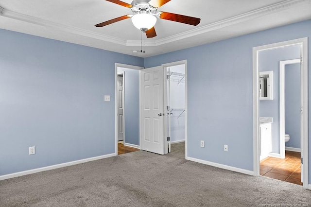 unfurnished bedroom featuring carpet flooring, a walk in closet, crown molding, and baseboards