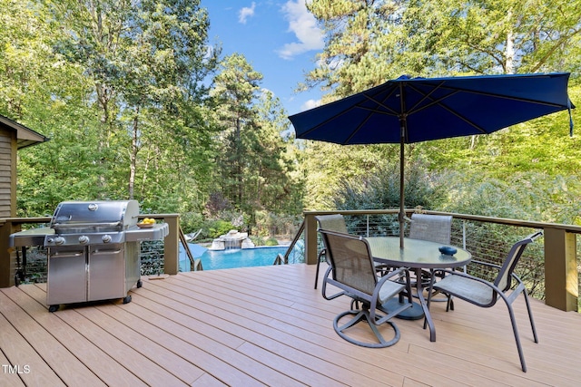 wooden terrace featuring outdoor dining space, an outdoor pool, a forest view, and area for grilling