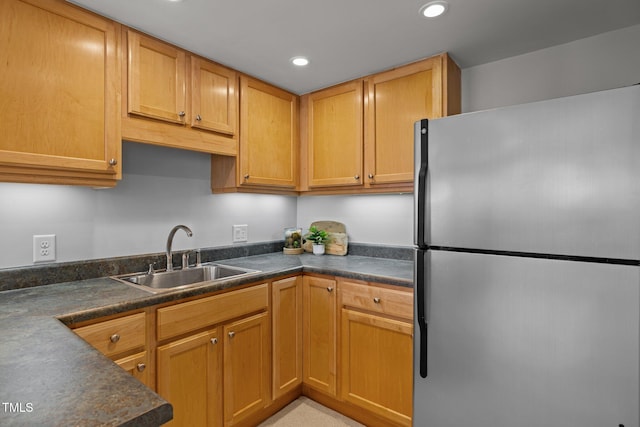 kitchen featuring dark countertops, recessed lighting, freestanding refrigerator, and a sink