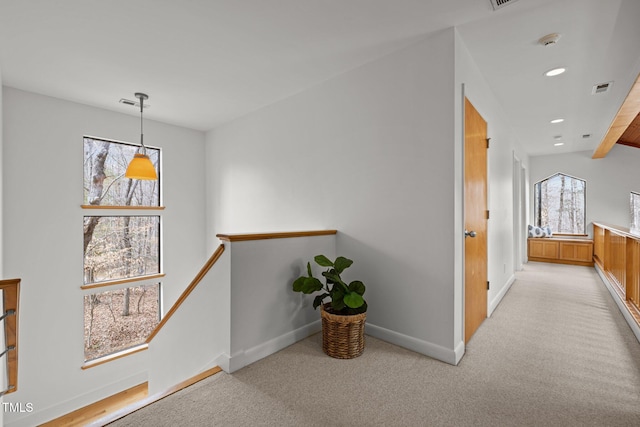 hallway with visible vents, an upstairs landing, light colored carpet, and baseboards